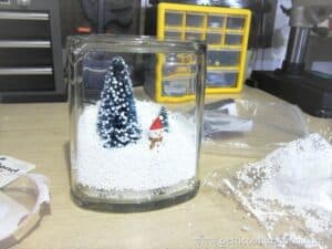 making a snow scene in a glass jar with snowman, snow, and trees