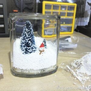 making a snow scene in a glass jar with snowman, snow, and trees