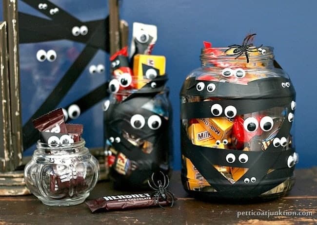 Googly eye and black electrical tape decorated Halloween candy jars.