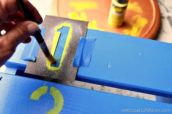 stenciling yellow numbers on a step stool