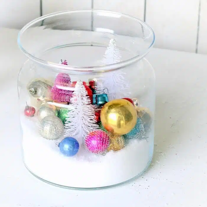 How to make a diy snow scene in a large glass container using bottle brush trees and Christmas ornaments