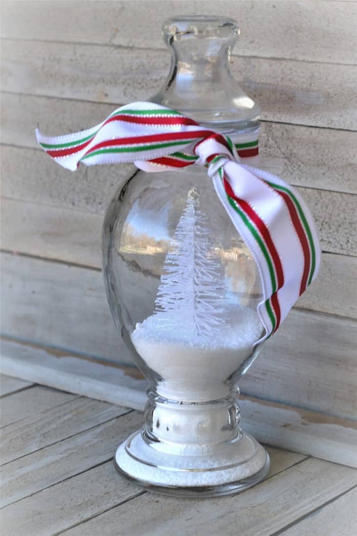 glass vase with lid contains a minature white bristle brush Christmas tree and Epsom Salt for snow