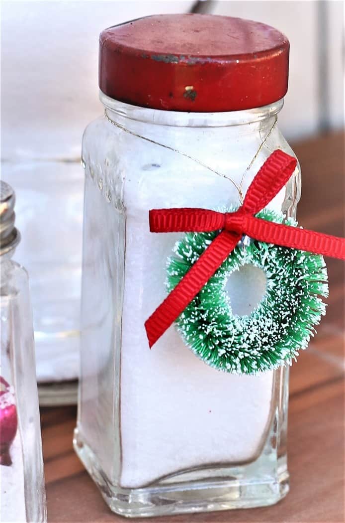 vintage mini spice bottle with red lid and filled with fake snow and tied with a mini wreath ornament