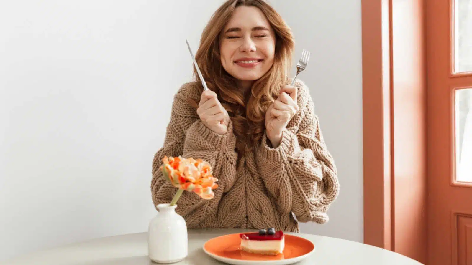 Portrait of an excited woman in sweater getting ready to eat cheesecake on a plate at the table