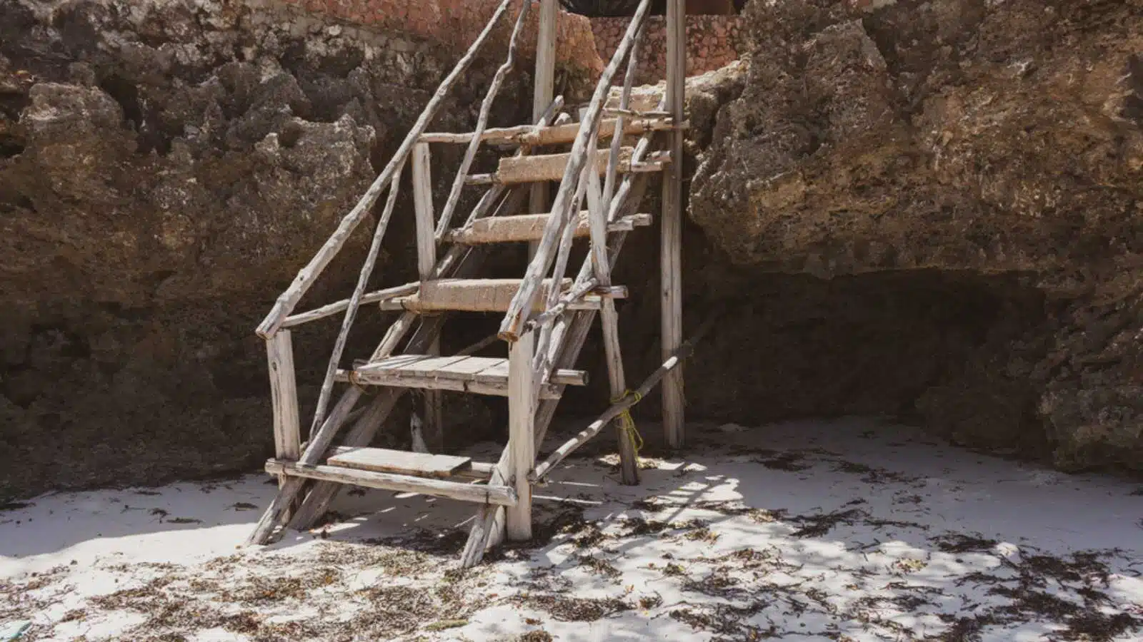 Old wooden staircase on the beach. Rustic ladder in stones on tropical beach. Ancient stairs on the rock. Architecture details in tropical village.