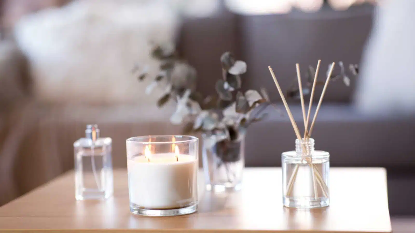 decoration, hygge and aromatherapy concept - aroma reed diffuser, burning candle, branches of eucalyptus populus and perfume on table at home