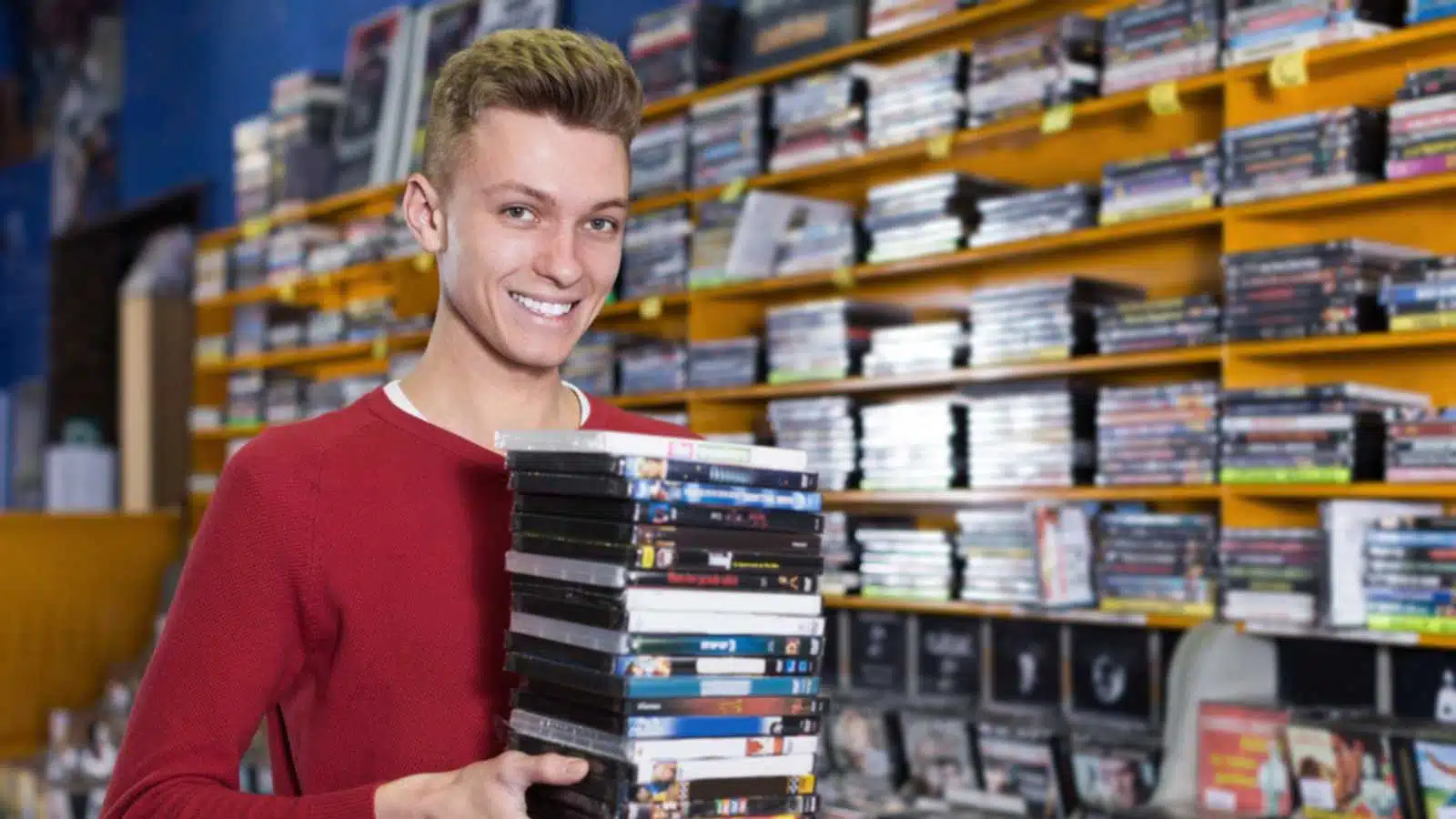 Portrait of smiling young guy customer holding stack of DVDs in shop
