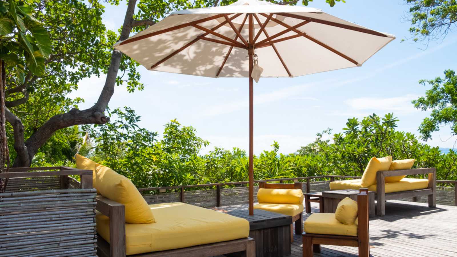 Wooden, yellow sofa couch with umbrella at the outdoor patio. With green tree and blue sky nature background.